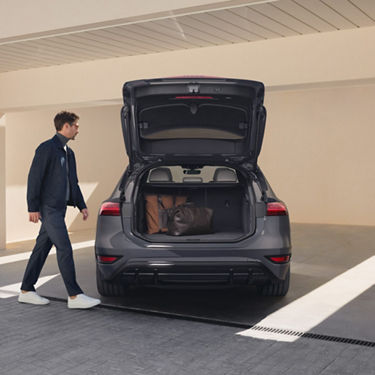 Person walking past an open car trunk with luggage inside.