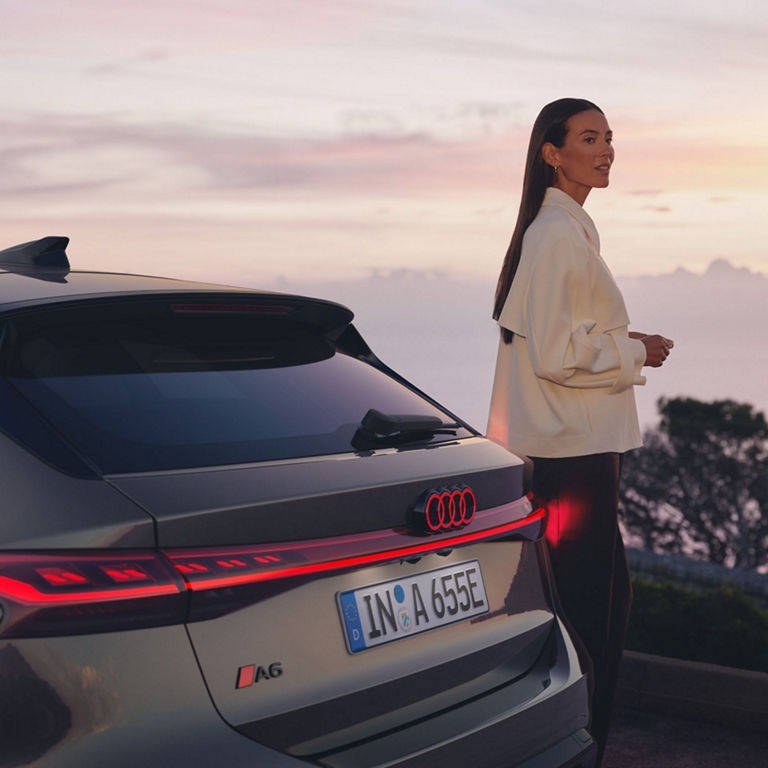 Person standing next to an Audi car at sunset.