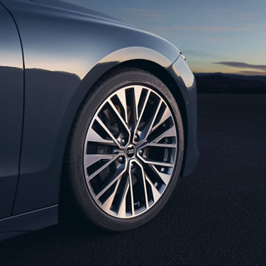 Close-up of a car's alloy wheel with a logo, at dusk with a soft sky background.