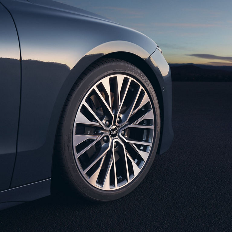 Close-up of a car's alloy wheel with a logo, at dusk with a soft sky background.