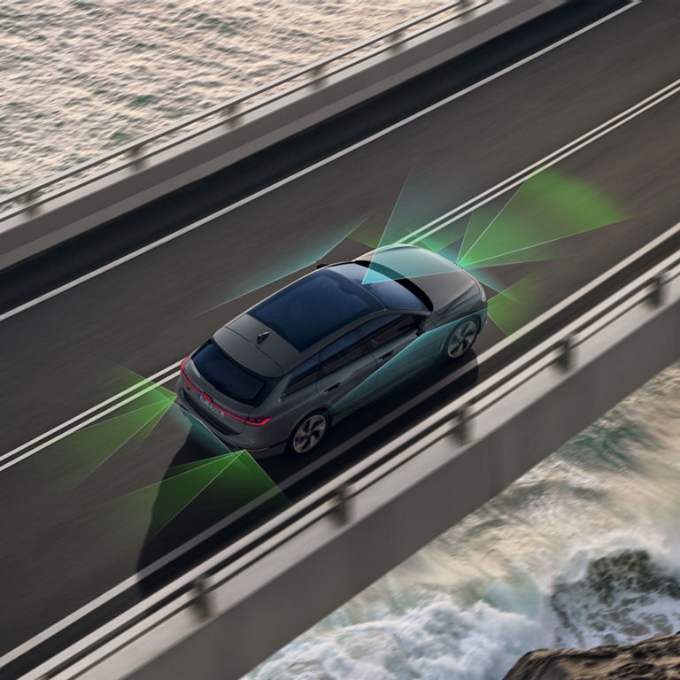 Car driving over a bridge with sensor visualization graphics on a coastal road.