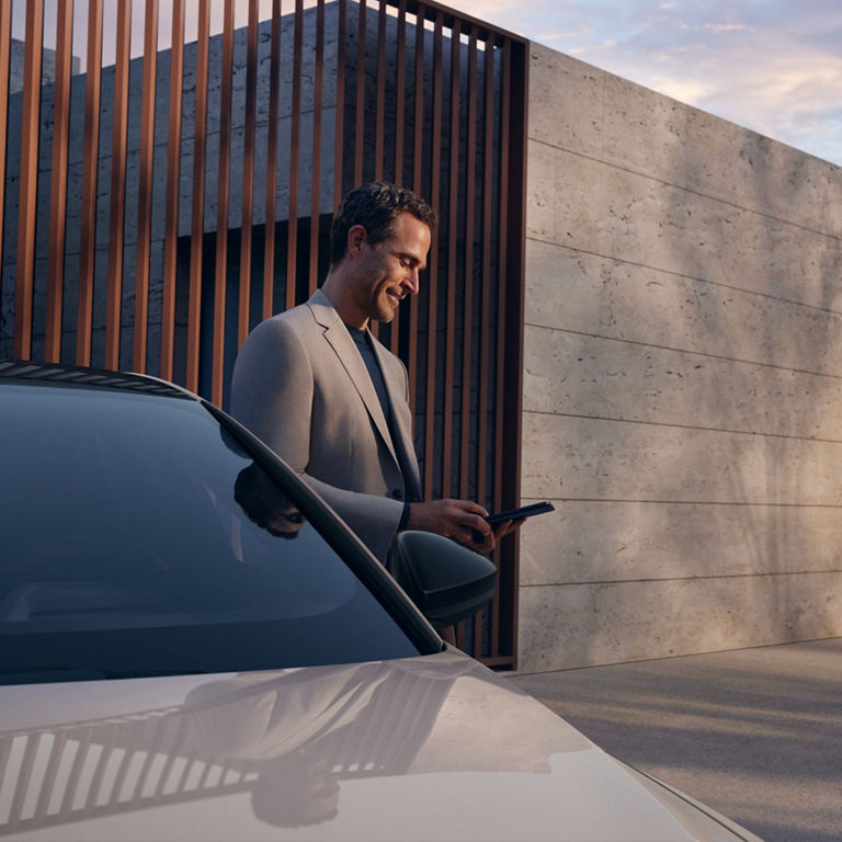 Person in a suit by a car with a phone in hand near a modern building.