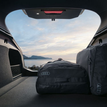 View from inside a car trunk with bags, facing a sea horizon at dusk.