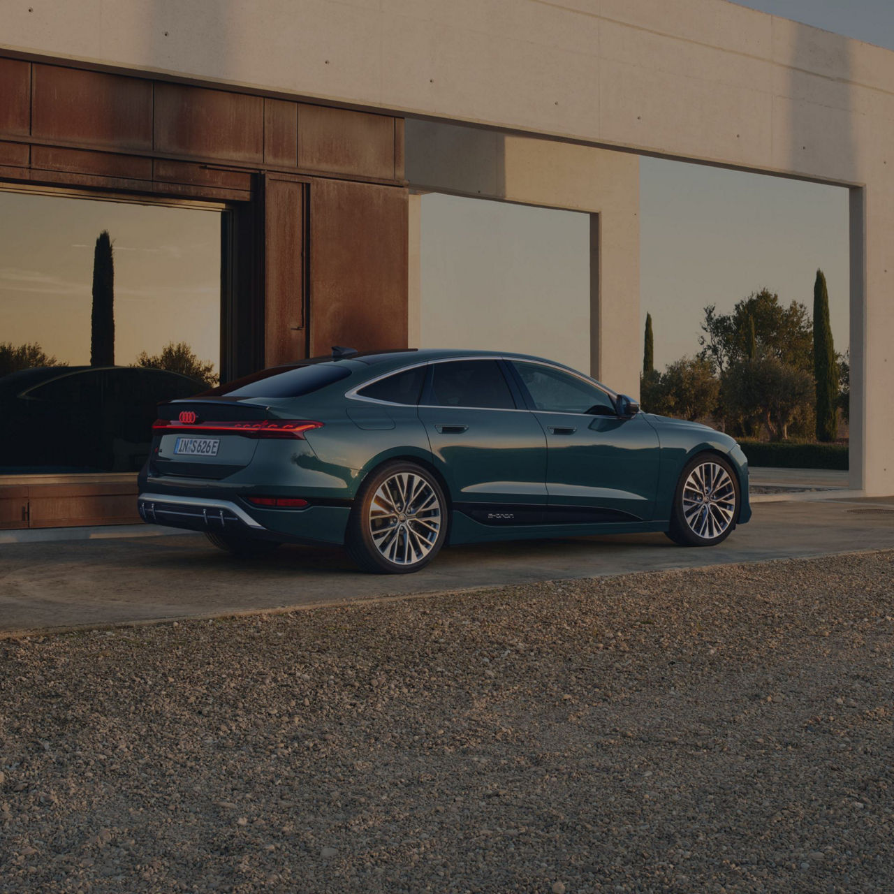 A dark colour sedan parked outside a modern building at dusk.