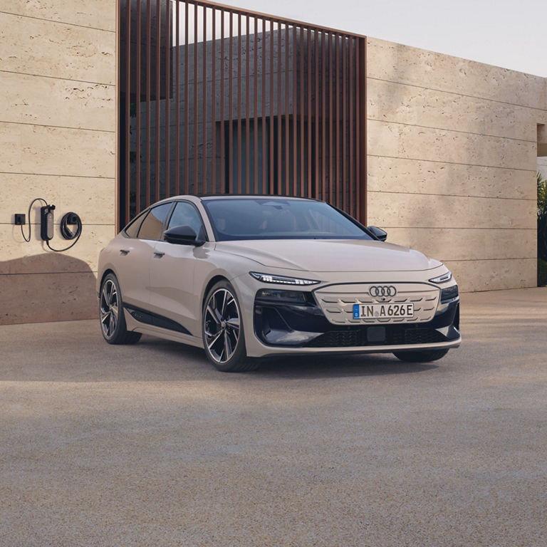 A white Audi electric car parked beside a wall with a charging station.