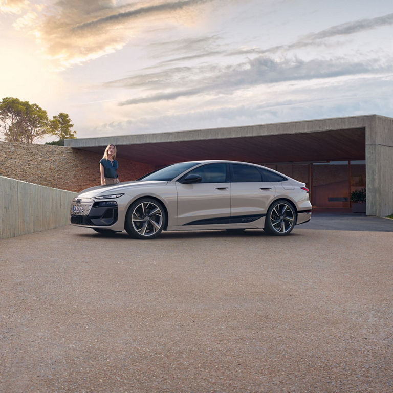 A white sedan parked outside a contemporary building with a person standing by the car.