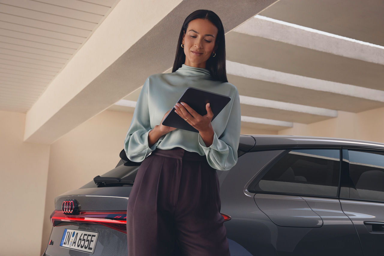 Person holding and looking at the tab while standing beside a car.