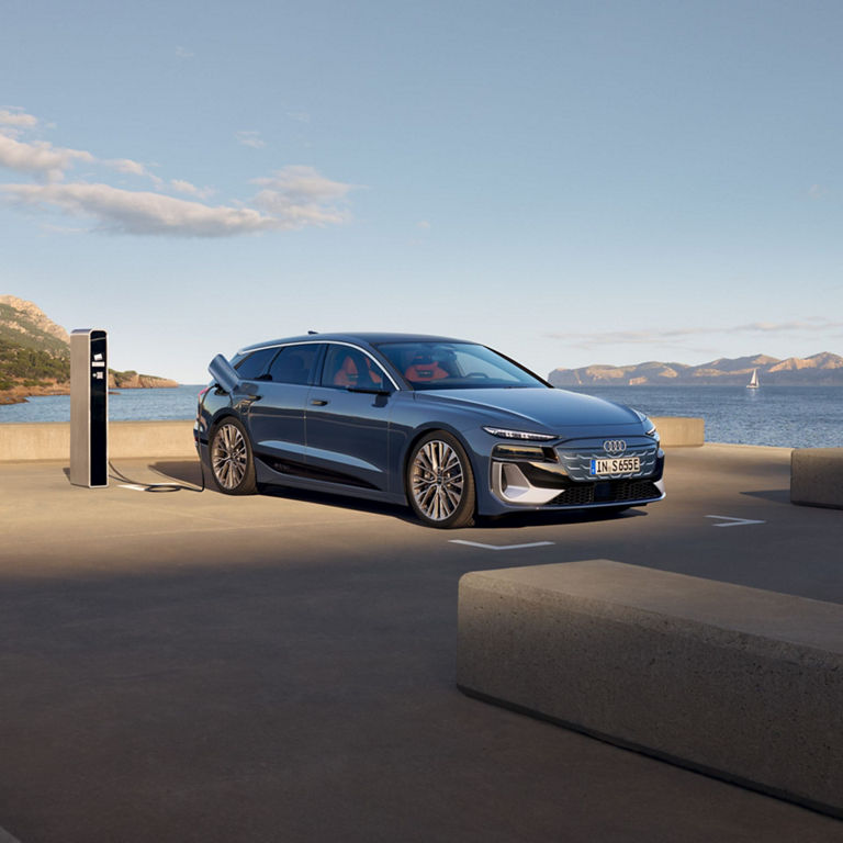 Audi electric car charging at a station by the sea with mountains in the background.