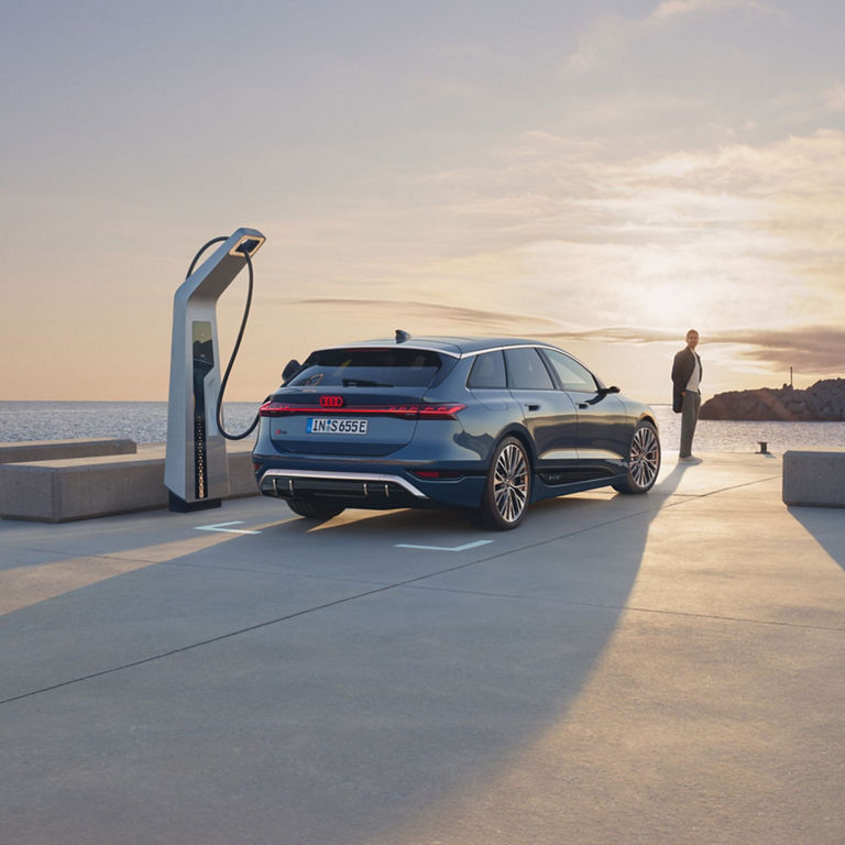 Audi electric car charging at a station during sunset.