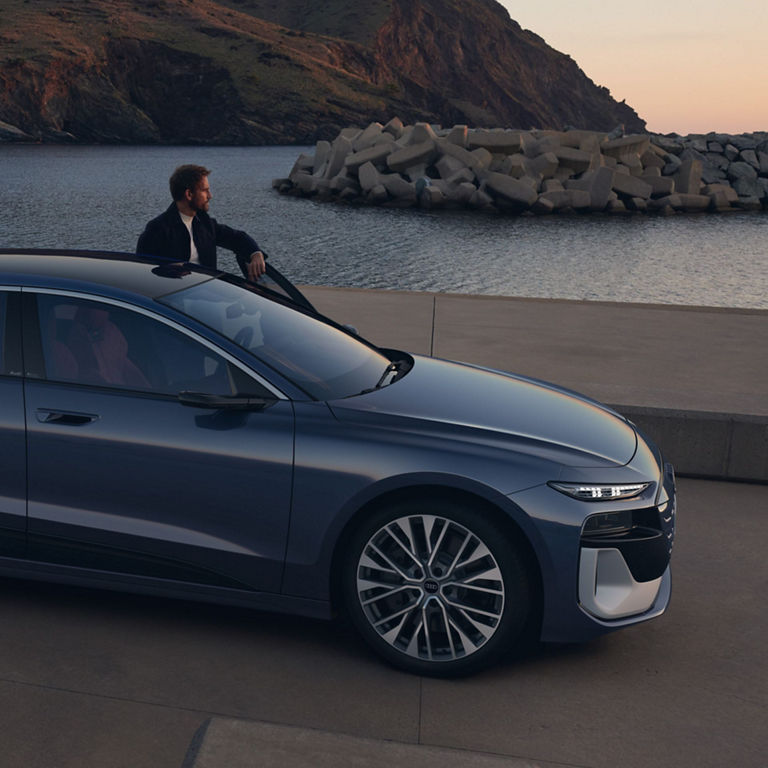 Car parked by a seaside with hills in the background during dusk.