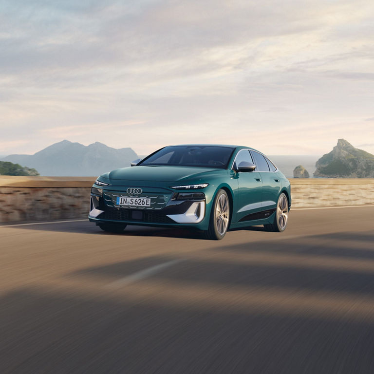 A teal Audi car driving on a coastal road with mountains in the background.