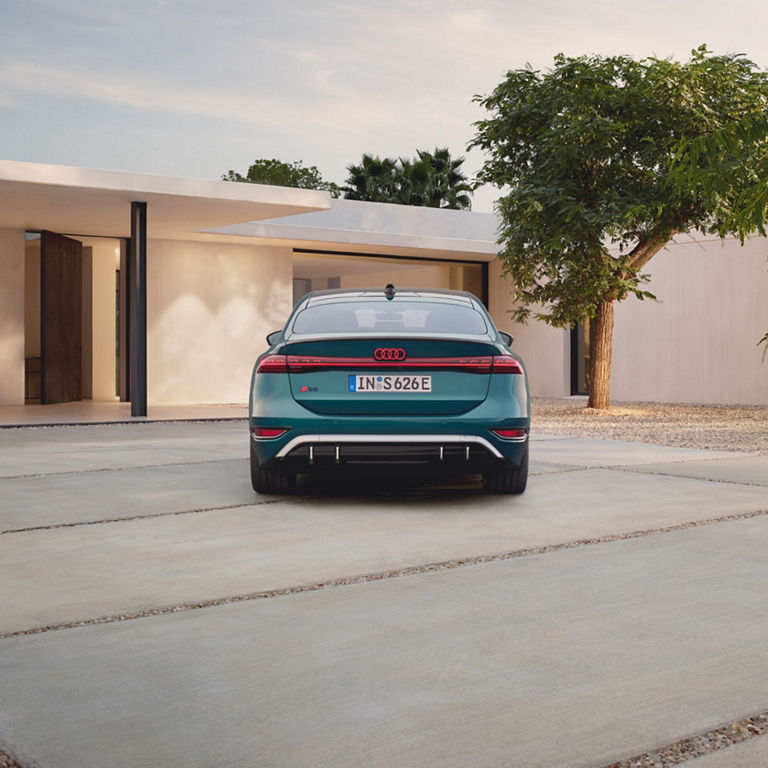 A teal Audi S6 e-tron Sportback parked outside a modern house with a minimalistic facade.