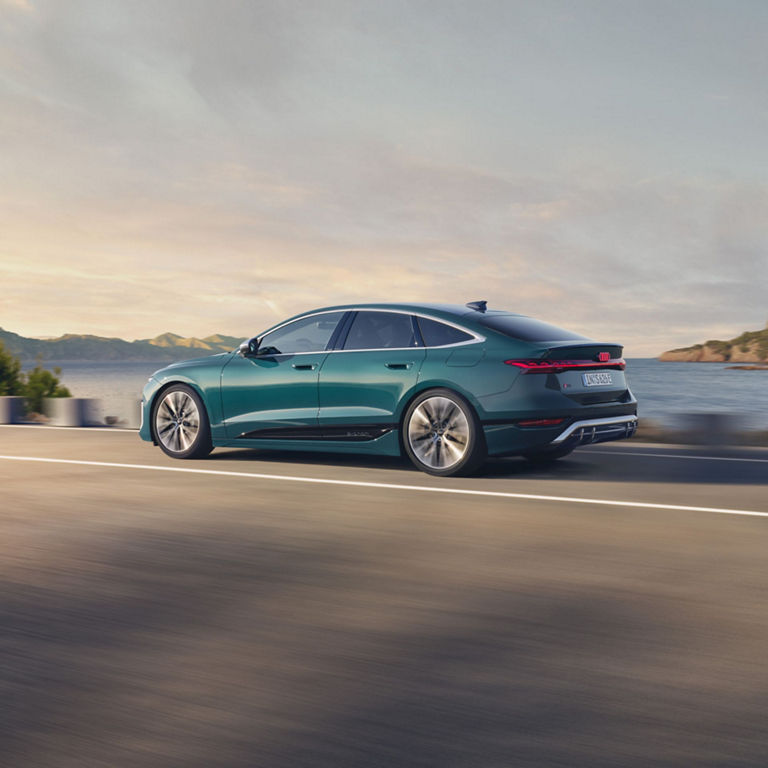 A teal sedan driving along a coastal road.