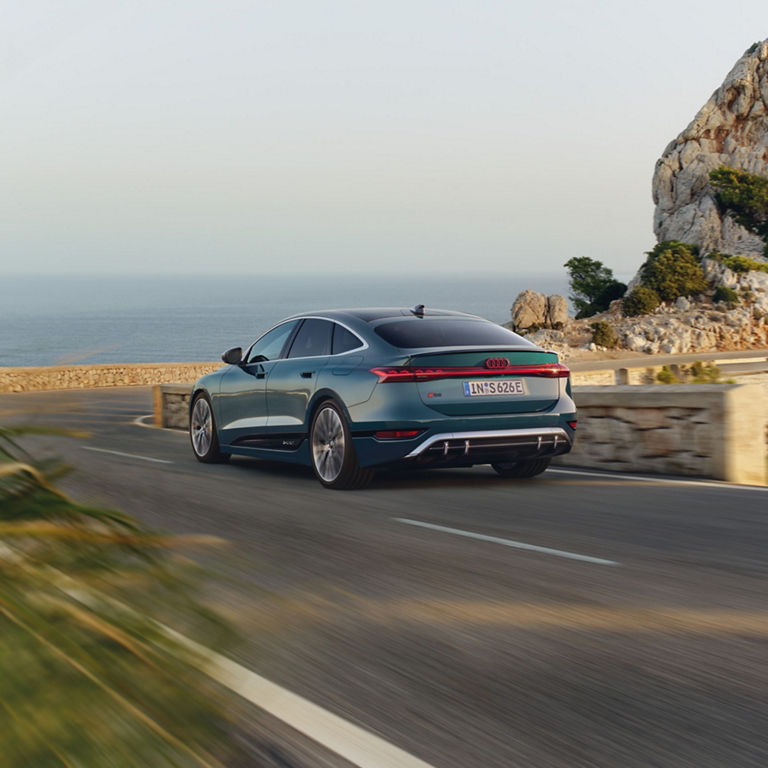 Sedan driving on a coastal road with scenic sea and cliffs in the background.