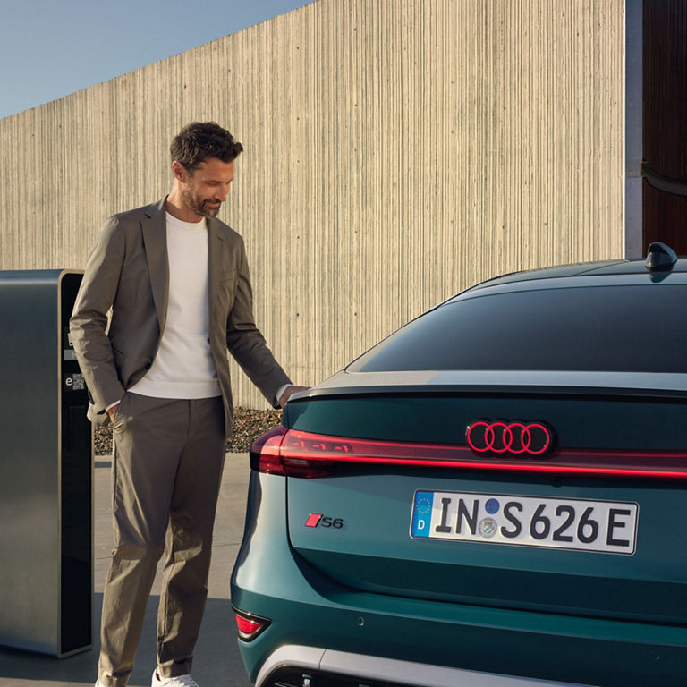 A person standing next to an Audi electric vehicle at a charging station.