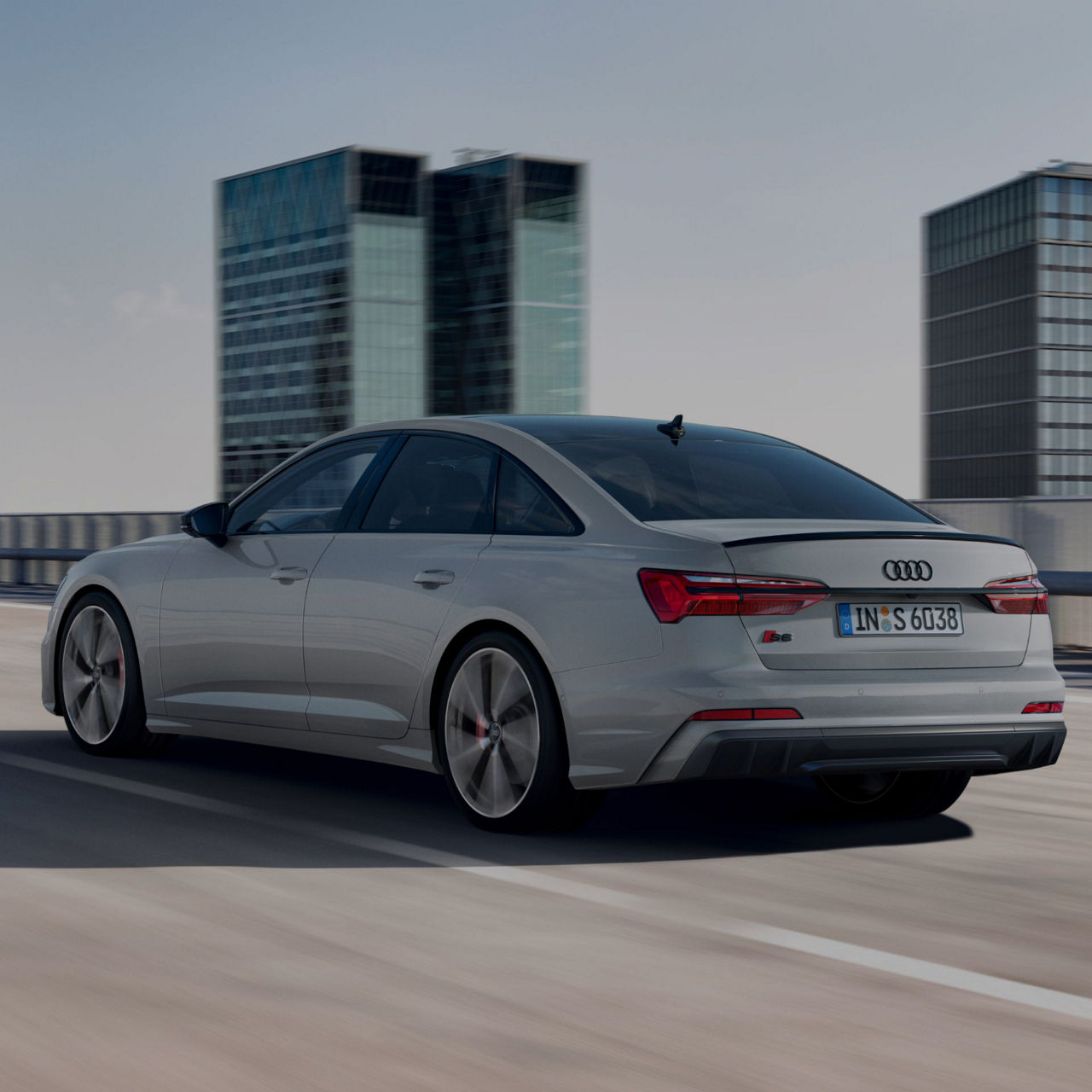 Sedan driving on a road with modern buildings in the background.