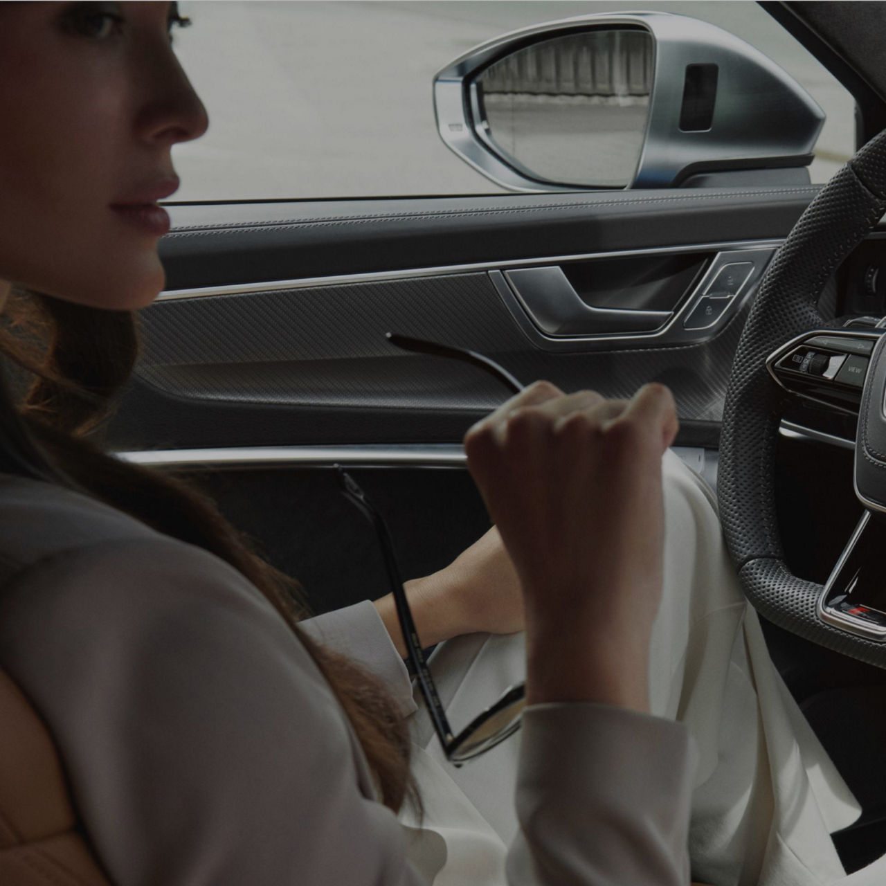 Person holding sunglasses inside a car with visible steering wheel and car door. 