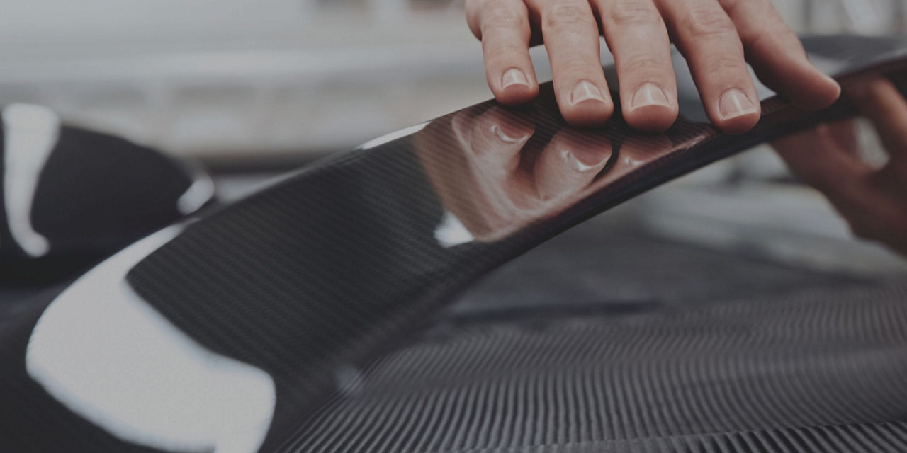 Close-up of a hand touching the carbon fiber protective film on an Audi car surface.