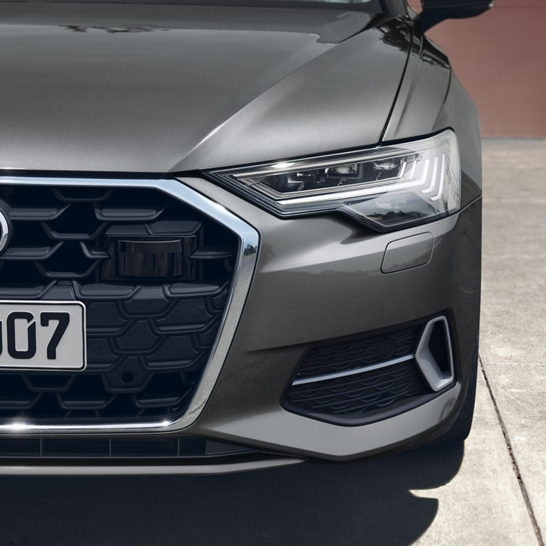 Close-up of a car's grille, headlight, and badge with a license plate.