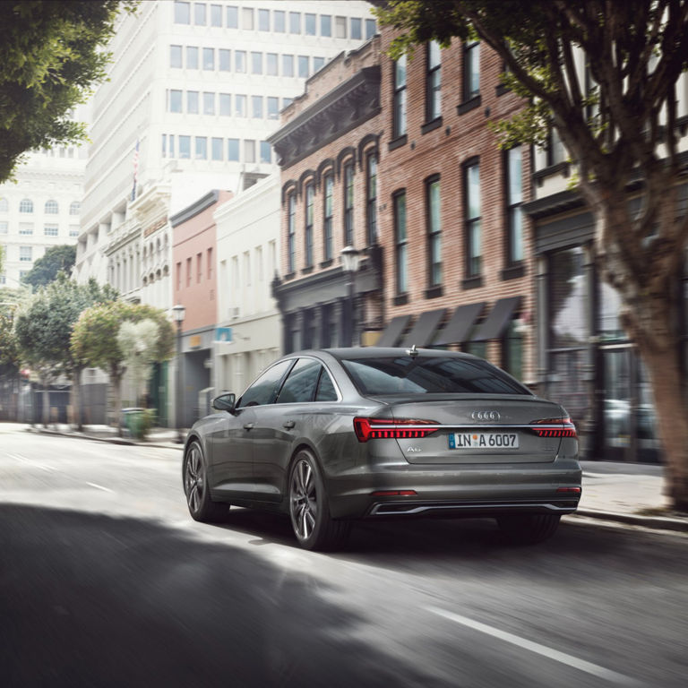 A light grey Audi car driving on a city street with motion blur effect.