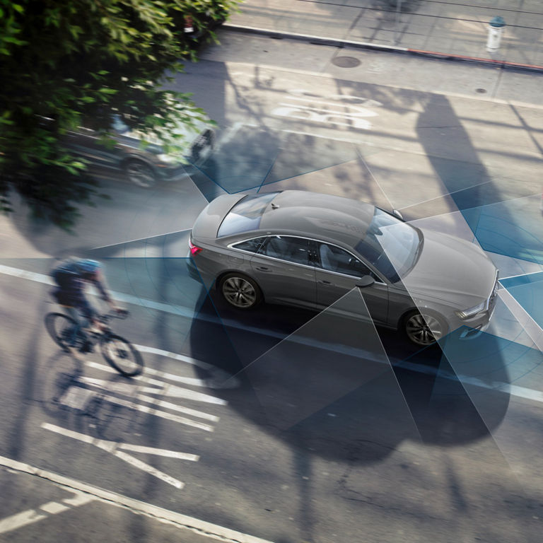 Aerial view of a car with sensor detection zones, near a cyclist on the street.