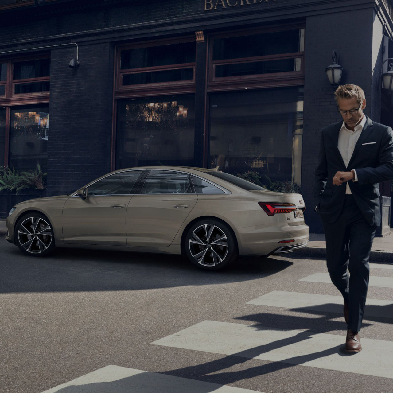 Man in a suit walking past a sedan parked on a city street.