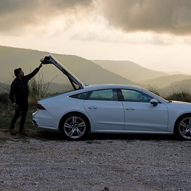 Person opening trunk of a white car on a cloudy day in a rural setting.