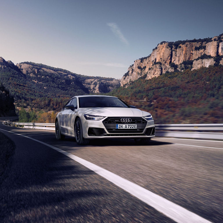 A white Audi driving along a scenic mountain road.