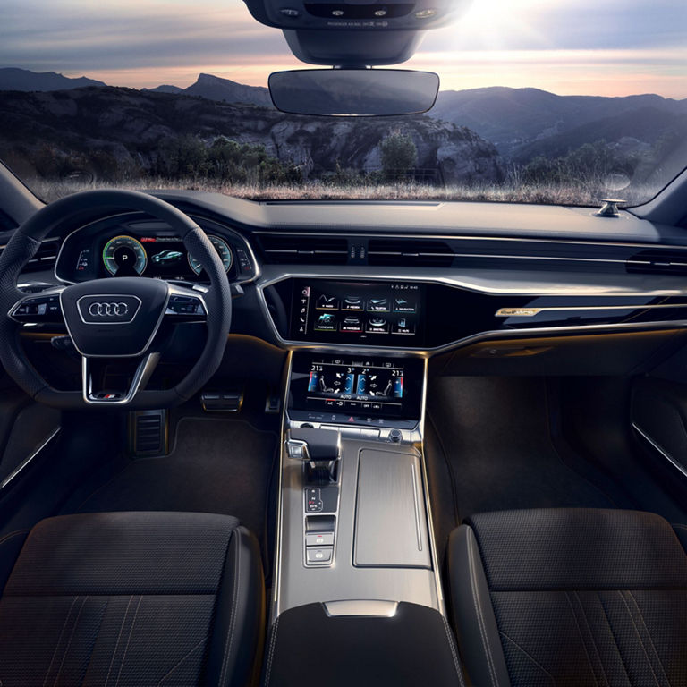 Car interior at dusk with leather seats, dual touchscreens, and a digital dashboard.