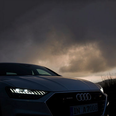 Audi car front view with lit headlights under a moody sky.