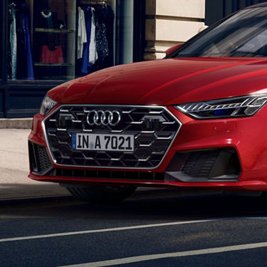 Red Audi car front close-up with European license plate, parked by a clothing store.