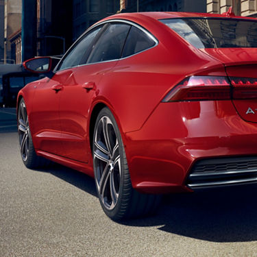 A red sedan parked on a city street, with a sleek design and modern alloy wheels.