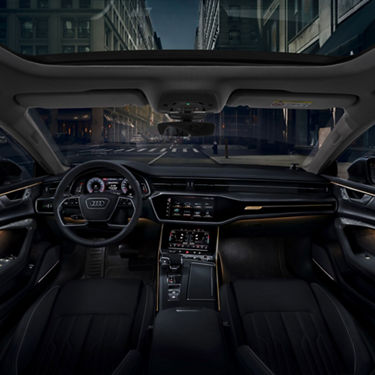 Interior view of an Audi car with dashboard, steering, and city street ahead.