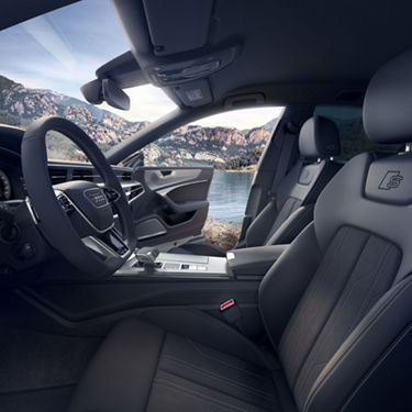 Interior view of a car with steering wheel and dashboard, overlooking a lake and mountains.