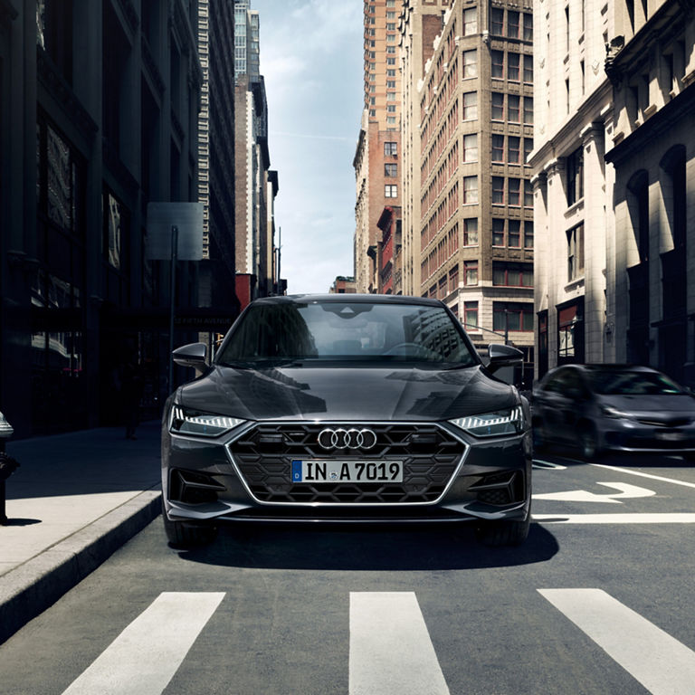 An Audi car parked on a city street with buildings and a pedestrian crossing.