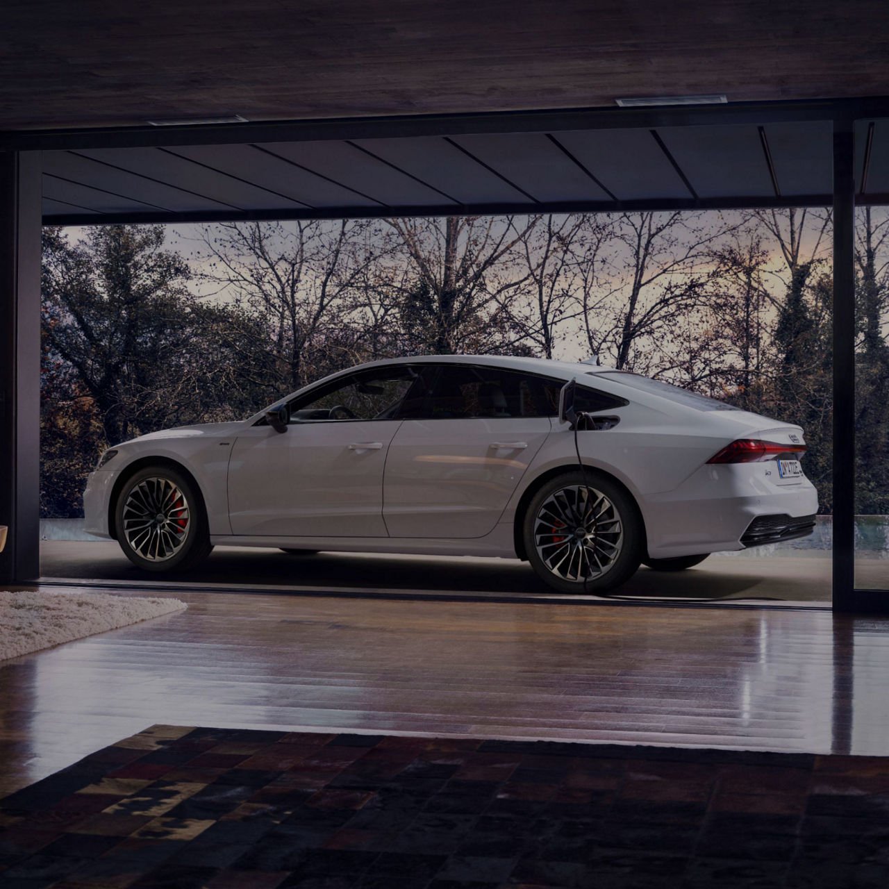 White sedan parked inside a modern garage with glass walls and trees outside.