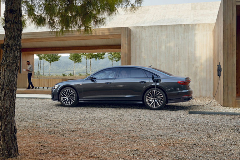 A black sedan charging at an outdoor station, with a modern wooden building in the background.