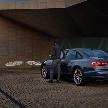 A man in a suit opening the door of a modern sedan under a building overhang.