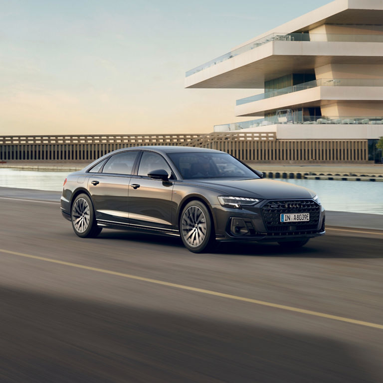 A sedan driving by modern architecture near water.