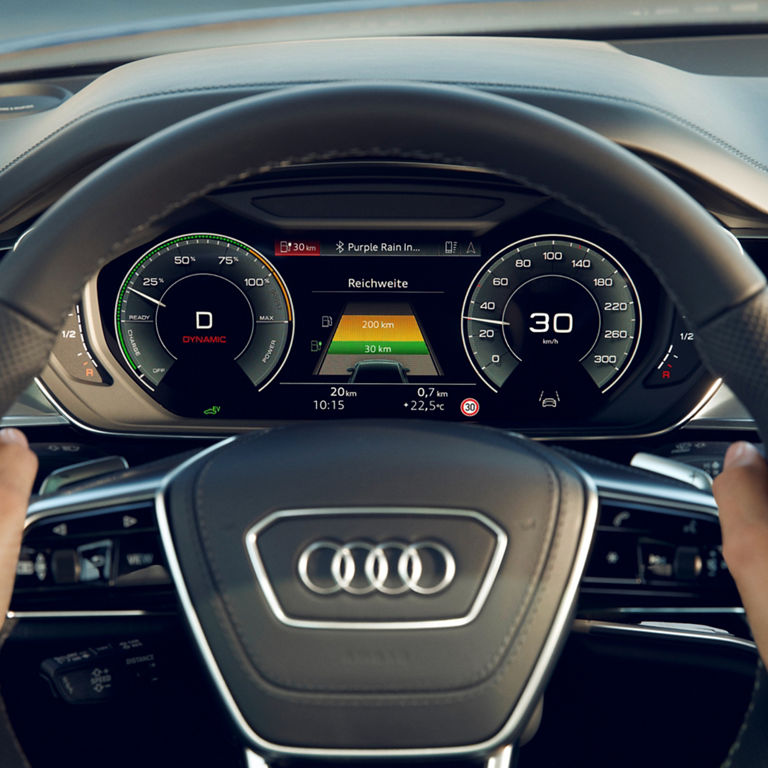 Driver's perspective of an Audi's steering wheel and digital dashboard displaying speed and battery range.