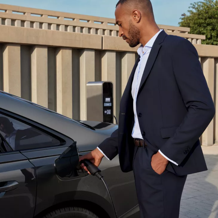 Person in a suit charging an electric car at a charging station.