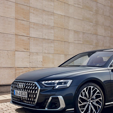 Blue Audi car parked in front of a beige stone wall.