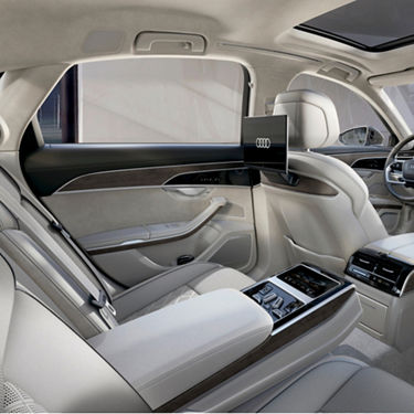 Car interior with leather seats and wood accents, displaying Audi logo on screen.