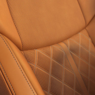 Close-up of a tan leather car seat with perforated and stitched detailing.