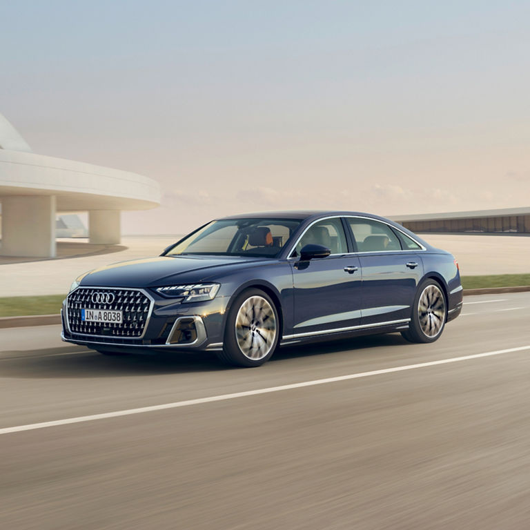 A  Audi sedan driving on the road with a modern building in the background.