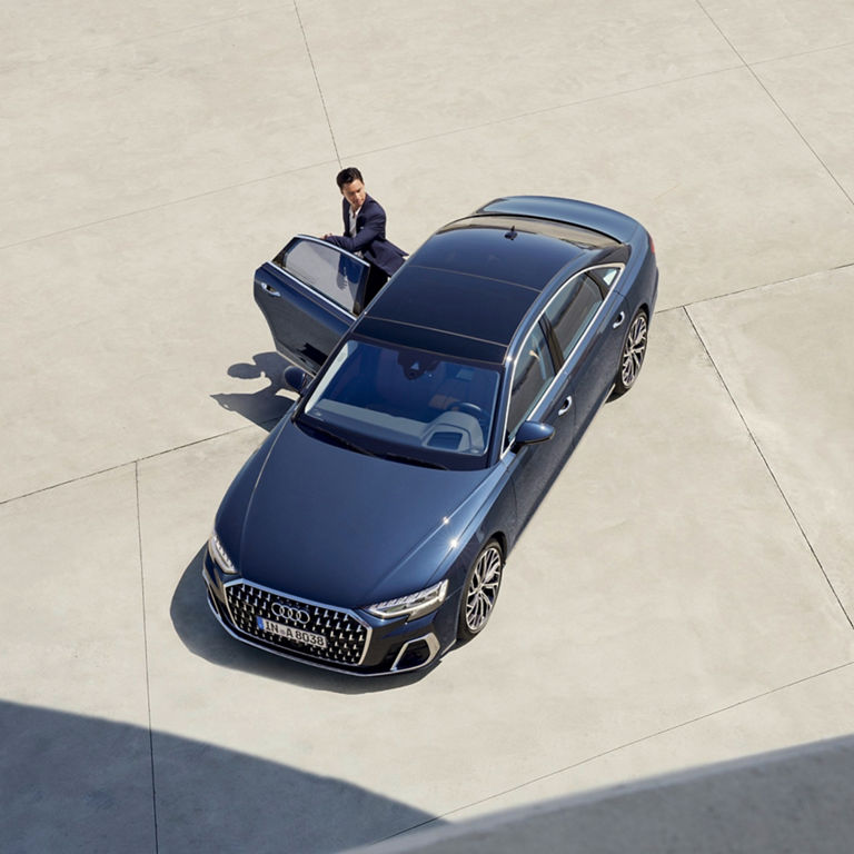 Aerial view of a person standing next to an open door of a parked blue sedan.