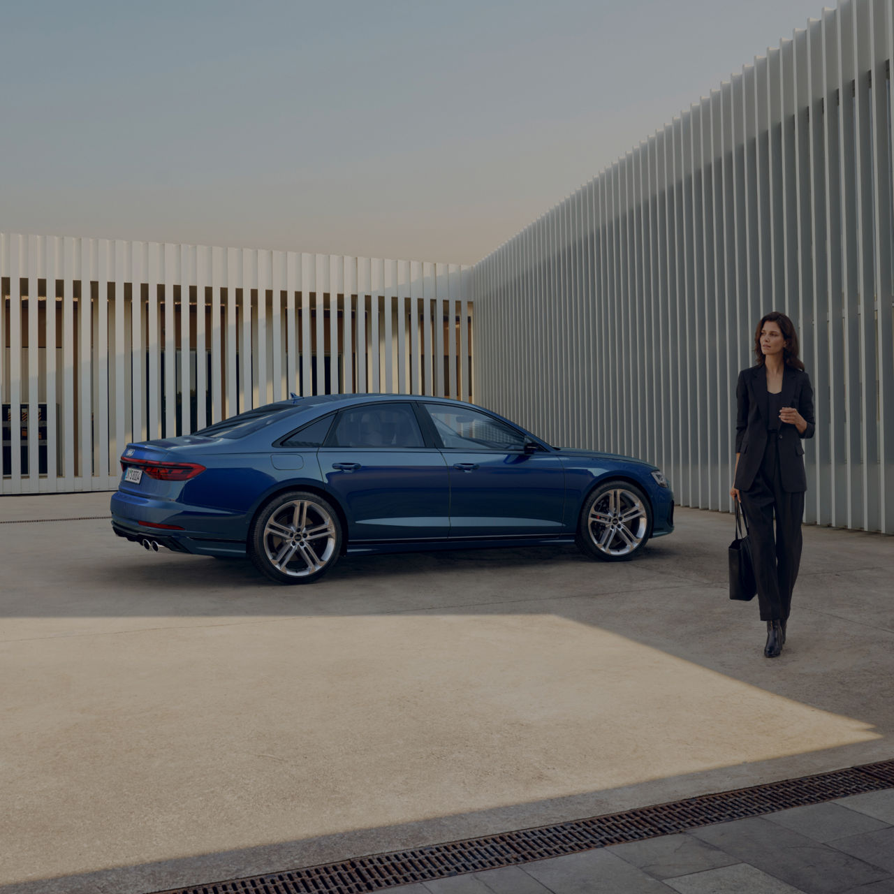 A blue sedan parked next to a modern building with a person walking by.