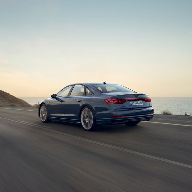 Audi A8 driving along a coastal road at dusk.