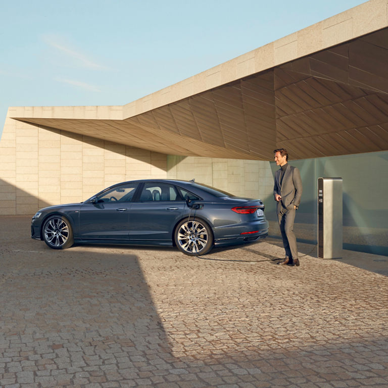 A sedan parked at an electric charging station with a modern building in the background.