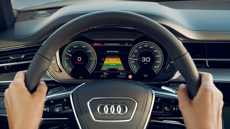 Driver's view of an Audi steering wheel and digital dashboard displaying vehicle information.